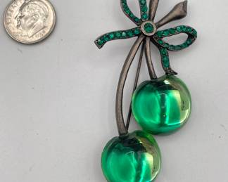 Maria Loran green glass cherry brooch with rhinestones, brushed metal frame, green rhinestone bow tied at top of the cherry stems. The pin is stamped on the back Loran in a crown. 
