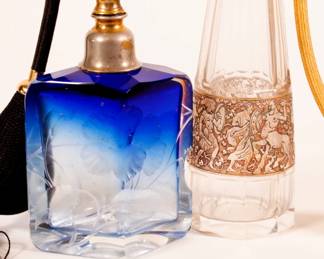 Closeup of pair of antique Art Nouveau era Moser Bohemian art glass perfume bottles with atomizer tops, one with gilt mythological warrior surround, the other a clear to blue rhomboid shape, crystal body deeply engraved with blooms and leafy stems
