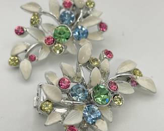 Closeup of pair of BSK clip earrings, silver tone metal with white enamel leaf shapes and jewel cut glass pieces in pink, ice blue, and spring green