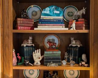 One of two bookshelves in the great room area, with vintage books, bookshelf lamps, antique English porcelain plates, cast iron toys, Mottahedeh cats and glass marble collections.