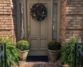 Very inviting front door with fruity wreath, thoughtfully lightweight pair of faux terra cotta planters with yellow mums and another pair with healthy Boston ferns.