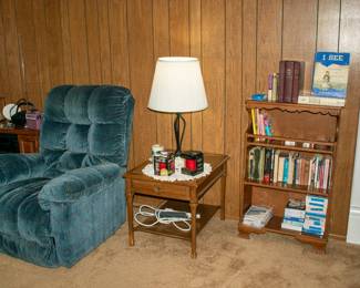Nice recliner chair, side table, bookshelf, books, greeting cards, lamp.