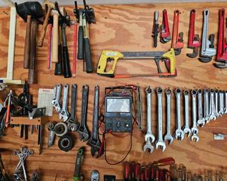 Hack saw and pipe cutter wrenches and more hanging on the wall over workbench