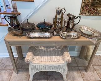 Silver plate pieces atop a whitewash sofa table and white wicker seat