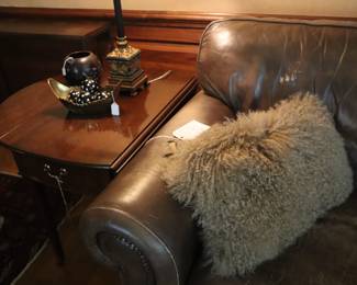 Mahogany pembroke table next to a well made sofa  that the leather has worn.  Very worth getting reupholstered in fabric. Fuzzy pillows, Den