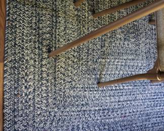 At woven navy and white rug, approximately 4 x 6. Has a denim look, on the landing under a card table and folding chairs.  