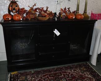 A black media cabinet with glass doors so that a remote control will work on devices. The length is great for today's large TVs to be above on wall or sit on it. In the north entrance room. 