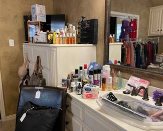 The bathroom has lots of shampoos, lotions, perfume, hair appliances, and makeup 