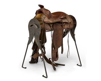 93
A Guy Gooding leather cutting saddle on iron stand
Early 20th century
Marked to seat: Guy Gooding / Maker / San Bernadino Cal; stand marked: Fontanini
The ranch-style tooled leather saddle with foliate and acorn motifs, featuring open stirrups, tie-on straps to front and rear with silvered metal grommets, front and rear cinches, wool woven girth strap, and fleece lining, set on a black enameled wrought iron stand
Seat: 16"; Gullet width: 13"; Stand: 38" H x 37" W x 27" D
Estimate: $600 - $800