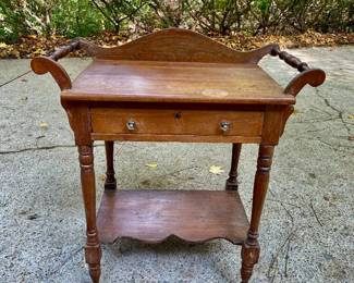 Lot 026-GAR: Antique Wash Stand

Features: 
•	Featuring turned side handles/rungs, a single storage drawer, and a lower display shelf with a scalloped edge. The backsplash and delicate turned legs enhance its antique appeal. With its warm, rustic finish, this piece can serve as a charming accent table or entryway piece, and it can add rustic character to any space. The key is lost.

Dimensions: With the handles: 28.5”W x 17.75”D x 33”H


Condition: Good pre-owned condition. Some water marks seen on top surface from a glass, and overall finish is worn. See pictures for more detail.
