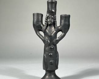 FIGURAL POTTERY CANDLESTICK | An unusual figural pottery candle stick holder of modern style designed as a female figure with feathers on her dress, her hair in braids; no apparent signature or marking. - h. 10.25 x w. 4.75 in