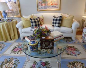 White sofa, lucite & glass top round coffee table, skirted side table, bric-a-brac, needlepoint area rug