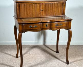 JOHN WIDDICOMB LADY'S WRITING DESK, OAK WITH ROLLER FRONT | The desk features a roller front with ribbed wood tambour door, which opens to reveal compartments and drawers for organizing stationary and writing materials. Below, a sculpted front drawer is adorned with brass hardware. The desk is supported by four cabriole legs, which are characteristic of traditional French-style furniture. A leather insert on the writing surface enhances its functionality. Drawer interior marked: "John Widdicomb Makers of Fine Furniture, Grand Rapids, Michigan." - h. 39.5 x w. 32 x d. 19 in