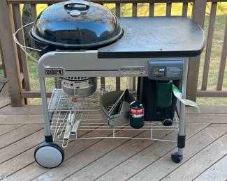 WEBER PERFORMER CHARCOAL GRILL | Round Weber charcoal grill with built-in propane ignition, metal top, and charcoal storage bin all together on a rolling frame. - h. 46 x w. 29 x l. 48 in