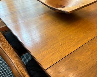 Closer view of the surface of the dining table with six wood and cane chairs and two leaves.