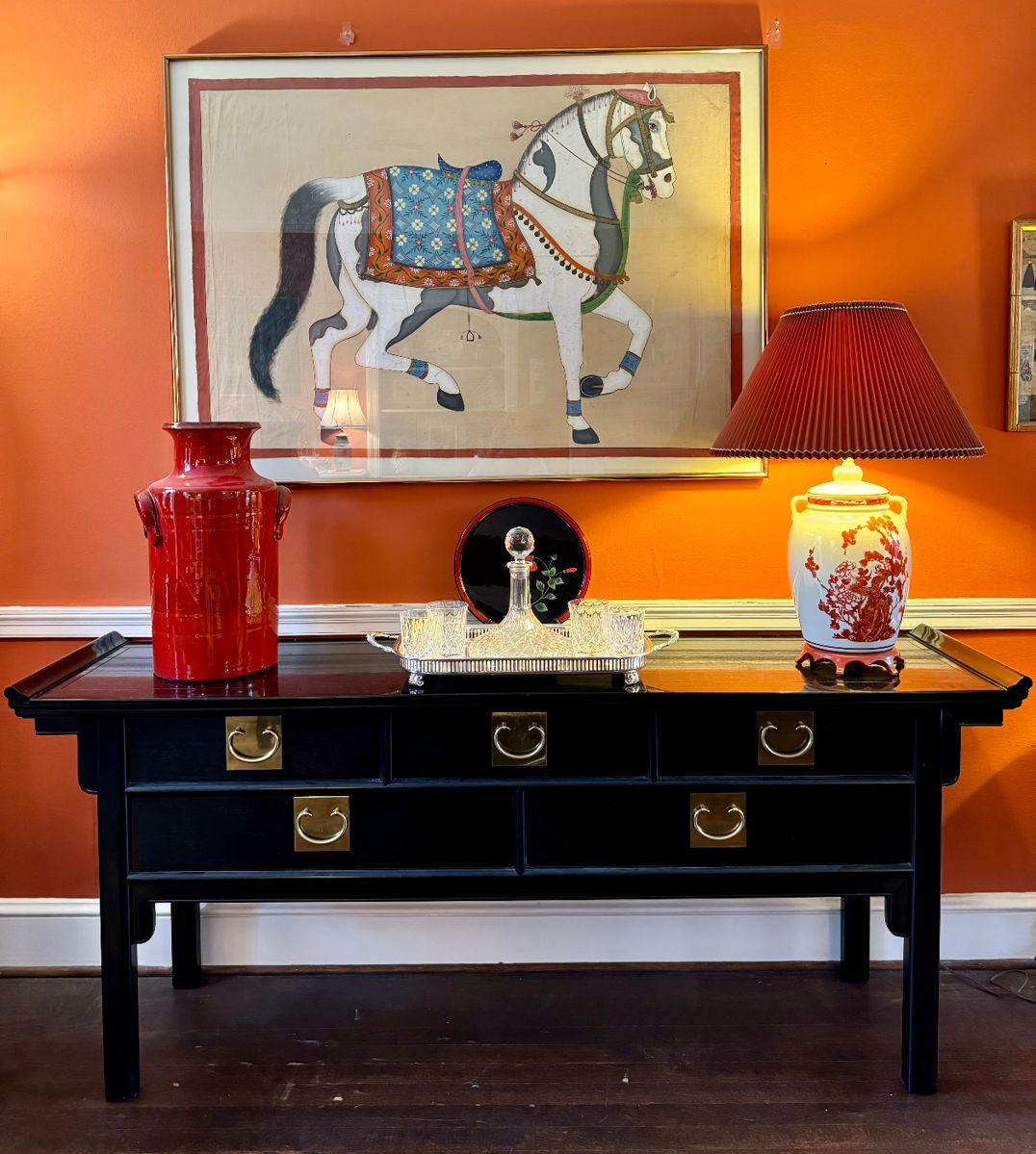 $850; original, hand-painted horse on fabric in gold frame; 51.5x37.         SOLD—orange glazed large ceramic vase; 19.5h.          $1500; Century brand 5-drawer pagoda style buffet with black finish and brass hardware; 72x18x31.          $56; lacquerware hibiscus tray with red trim and floral accent; 12”d.        $28; set of 4 rocks glasses.       $60; glass decanter.         $68; silver plated footed tray.          $250; ceramic palace jar lamp with peacock accents; 20x28