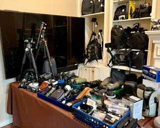 Table full of quality photography camera gear, tripods, camera bags, binoculars, etc. 