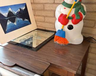 Snowman Decoration and Mountain Painting
A cheerful light-up snowman figure holding a broom, perfect for winter décor. Next to it is a striking painting of snowy mountain peaks reflected in a serene lake, adding an artistic touch. Also included is a wooden side table and rolled-up artwork.