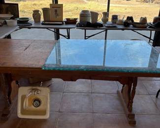 Rustic Wooden Table with Glass Top and Ceramics
A sturdy wooden table featuring a removable glass top, perfect for dining or as a workbench. The surrounding items include ceramic and pottery pieces, pitchers, and vintage-inspired artwork.