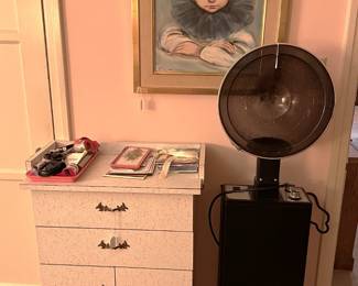 This a different view of the painting, short cabinet, and salon hair dryer.