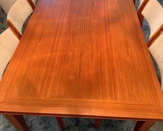 A pristine teak table with pull-out sides and six vintage teak chairs in perfect condition
