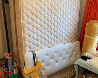 Full size bed with white padded headboard and mattresses and frame with some purses