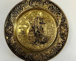A vintage brass wall plate featuring an embossed sailing ship design.