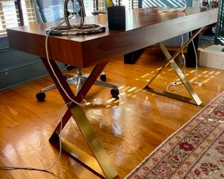 Jonathan Adler Channing Walnut and Brass Writing Desk.  Transform your workspace with the exquisite Jonathan Adler Channing Walnut and Brass Writing Desk. This piece seamlessly blends mid-century modern design with contemporary flair, featuring a  rich walnut finish that exudes warmth and sophistication. The sleek brass Neo-Classical brass crisscrossed legs add a touch of glamour, creating a visually striking focal point in any room.