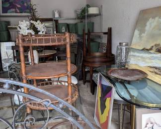 View of multiple items for sale: Decorative (refinished) Round Metal Wall Art / Brass Pea Shaped Desk with Matching Shape Beveled Edge Glass Top / Round Wicker 3 Shelf End Table with Leather Strapping / Pair of Wood SofaTables / Wall Art / Lighting / Faux Plants, etc