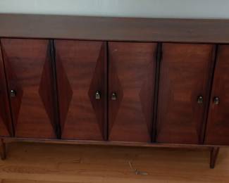Ramseur Walnut Bowtie Dresser
This walnut sideboard was made in the USA in the 1960s and features a diamond design on the front doors, three drawers by the 
middle door, top drawer used for utensils, 
and two interior shelves behind the left and
 right side doors.

Good Condition, Original Condition 
Unaltered, Some Imperfections Wear 
consistent with age and use.


66”w x 19”d x 32.5”h