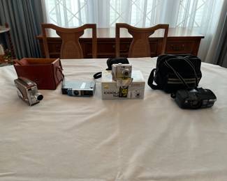 A collection of vintage cameras and hand-held video recorders, including Minolta, Keystone, DeJurette, and Nikon Coolpix.