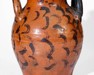 Fine Glazed Redware Jar with Profuse Manganese Swag Decoration, Eastern TN origin, early to mid 19th century, ovoid jar with semi-rounded rim and open loop handles, the lead-glazed surface extravagantly-decorated throughout with brushed manganese swags. One side includes a vertical foliate motif at the shoulder. Old black-painted wooden handle. Rim with a 1" smooth, shallow rim chip, some wear, and traces of old black paint. Chipping around foot. Surface wear. H 14". ($800-$1200)