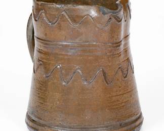 Small Brown-Glazed Stoneware Pitcher, attributed to the Decker Pottery, Washington County, TN, circa 1872-1910, tapering, tankard-form pitcher with footed base and raised banding to shoulder, featuring incised wavy line decoration to the collar and midsection. Surface covered in a chocolate-brown Albany slip glaze. Chips to spout. A 5/8" chip to interior of rim. A minor nick to exterior of rim. H 4 1/2". ($300-$500)
