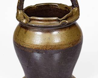 Salt-Glazed Stoneware Vase, Middle TN origin, late 19th or early 20th century, ovoid form with pronounced foot, horizontal strap handle, and two-tiered rim with pinched treatment, the surface dipped in reddish-brown slip and covered in a salt glaze. Provenance: Vase includes Wahler's handwritten note: "My 1st piece purchased in late 70's off the top of the water-melon man's truck at Labor Day Market for $15.00 in Monterey. His wife had purchased it in the twenties also." A 5/8" chip to bottom edge of rim and a few other minor rim nicks. H 10". ($250-$400)
