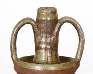 Salt-Glazed Stoneware Candlestick, Middle TN origin, late 19th or early 20th century, wheel-thrown candlestick with two open-strap handles and saucer base, dipped in reddish-brown slip and covered in a salt glaze. Provenance: Wahler's first "serious" purchase of Middle Tennessee stoneware: "Bought at the Crossville market.This was the start of my serious search for Md Tn pottery, although it was not my first piece." Excellent condition with wax residue. H 4 3/4". ($150-$250)
