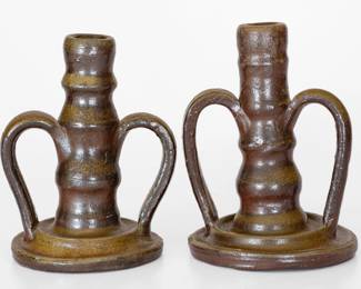 Two Salt-Glazed Stoneware Candlesticks, Middle TN origin, late 19th or early 20th century, a near pair of stylishly-turned sticks with open handles and tooled bases, each coated in a reddish-brown slip and covered in a salt glaze. Taller with one reglued handle and a small base chip. Shorter candlestick with one handle broken into three pieces and reglued, the opposite handle with one crack. H (of taller) 7". ($200-$300)
