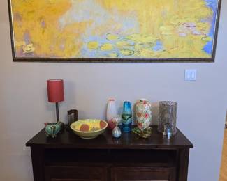 Large wall art piece along with other ceramic and glass art on a wood TV entertainment stand/cabinet