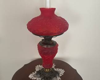 Lot 200 Red Satin Kerosene Parlor Lamp.  Fenton?  Beautiful red satin glass with leaf pattern, iron base.  Insert separates from base to light the way to bed at end of evening.  It is original, not converted to electric. Lamp measurements 27”h to top of clear chimney.  There is a crack in the shade at the top, see photos.   Beautiful lamp!