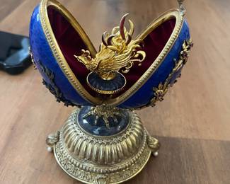 Large collection of faberge eggs reproduction of the Carl Faberge Firebird egg. Features a blue, guilloche, enamel egg decorated with floral studded tree branches set with natural red gems. The egg stands on a .925 sterling base with gold overlay, which has four scrolling feat with faux pearls on either side of each. The egg opens to a gold tone phoenix while playing music, and is lined in red velvet. The underside is marked "The Faberge Firebird Egg, House of Igor Carl Faberge, c. .87 FM., .925 Sterling". Measures 6 1/2" x 4". weighs 820 grams. $1000 no box