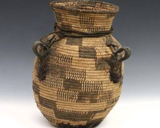 A turn of the century Native American basket olla, likely Apache.  Woven olla form with dyed geometric decoration, pine pitch lining and bottom with leather handles.  Some wear, pitch disintegrating.  9 1/2" high.  
