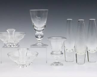 Seven pieces of 20th century Steuben Crystal tableware.  Includes three bud vases, an engraved chalice, a pair of low candlesticks and a urn form vase.  Each signed "Steuben".  Some surface wear.  Up to 8" high.  
