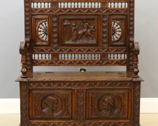 A late 19th century French hall bench from the Brittany region in northwest France.  Oak construction with hand carved rural scenes and spindlework detail features a shaped crest over a paneled back and shaped arm rests, lower boot well with hinged lid on short turned feet.  Original finish with minor wear.  44 x 17 x 59 1/2" high overall.  
