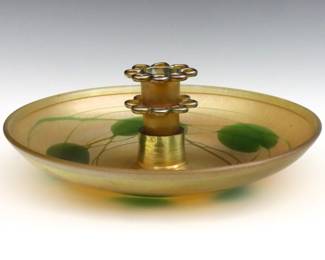 An early 20th century Tiffany Favrile glass center bowl with flower frog.  Circular form with flower frog insert, features trailing Lily Pad decoration on an Iridescent Gold ground.  Bowl and insert signed "L.C. Tiffany - Favrile" and "4663 K".  Fitter for insert has a very short crack and was previously ground down, minor surface wear.  13" diameter x 4 3/4" high overall.  
