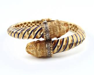 A Grecian 18k Gold bangle bracelet with Diamond accents and Lion design.  Hinged bangle with scrolled design features Lion head ends with Diamond chips accents prong set in White Gold and Blue enameled decoration.  Marked "750" with "Greece" and "3.37".  58.0 grams total.  Minor surface wear.  6" interior diameter.