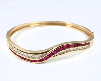 A 14k Gold, Ruby and Diamond bangle bracelet.  Hinged bangle with scrolled design featuring graduated channel set round cut Diamonds and square cut Rubies.  Marked "14k" and "GEI".  23.3 grams total.  Minor wear.  6 3/4" interior diameter.