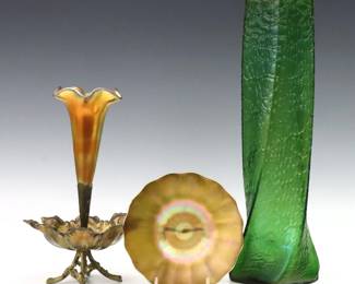 Three pieces of turn of the century Art Glass.  Includes an epergne with Iridescent Gold vase on a Gilded metal stand, a Bohemian Green vase with twisted design, and a Quezal Iridescent Gold dish with ruffled form.  Plate signed "Quezal".  Epergne base with minor distortion and wear to patina, Green vase with flakes to rim and foot.  Up to 15 1/4" high.