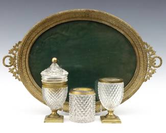 Four early 20th century French style vanity items.  Includes a French cut Crystal smoking set with table lighter and cigarette holder, a cut crystal jar with metal collar and an Empire style tray with silk lined bottom under glass.  Set marked "Made in France".  Mounts with wear to patina, smoking set lacks lighter insert, glass tray with some surface wear.  Up to 15" long and 6" high. 
