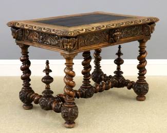 An 18th century Italian Renaissance style writing table.  Walnut construction with hand-carved and turned detail, features a turret top with inset leather and carved, molded edge above a skirt with single drawer decorated with scrolled foliate carving and Cherub mask pull flanked by Cherub mask corner blocks, Dragon end and foliate rear panels, supported by bold spiral turned legs, stretchers and center support, turned finials and carved feet with floral detail.  Old finish with good color, some wear and older replaced leather insert.  42 x 30 x 30" high overall.  
