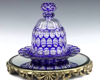 A 20th century glass serving dish and a mirrored tray.  Cut Cobalt to clear glass serving dish with scalloped tray and cloche, paired with a circular French style tray with mirrored bottom.  Glass and mirror with some surface wear, cloche with small flakes at rim, wear to tray's patina.  Serving dish is 11" diameter x 10" high, tray is 14 1/2" diameter.  
