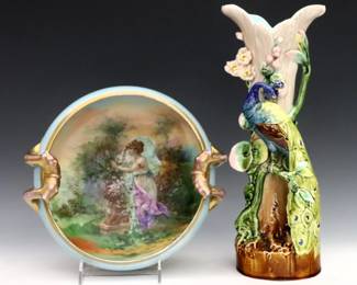 An early 20th century porcelain center bowl and vase.  Includes a handled Victoria Austria bowl with hand-painted scenic decoration and Gilded accents, and a Majolica floriform vase with Peacock figure.  Bowl with printed Victoria Austria mark used during 1904-1918, vase impressed "71" and "1946".  Bowl with some wear to surface and decoration, vase with crazing and firing crack to one of peacock's legs.  9" diameter and 13" high. 
